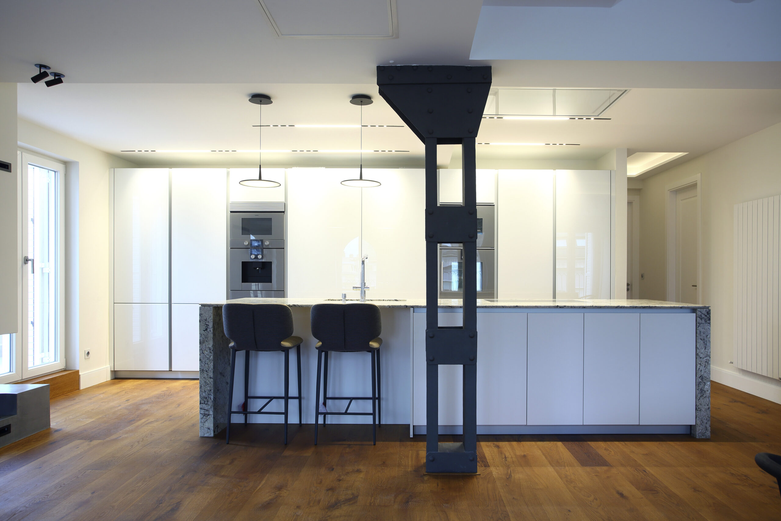 Cocina con isla, taburetes y campana central revestida en pladur