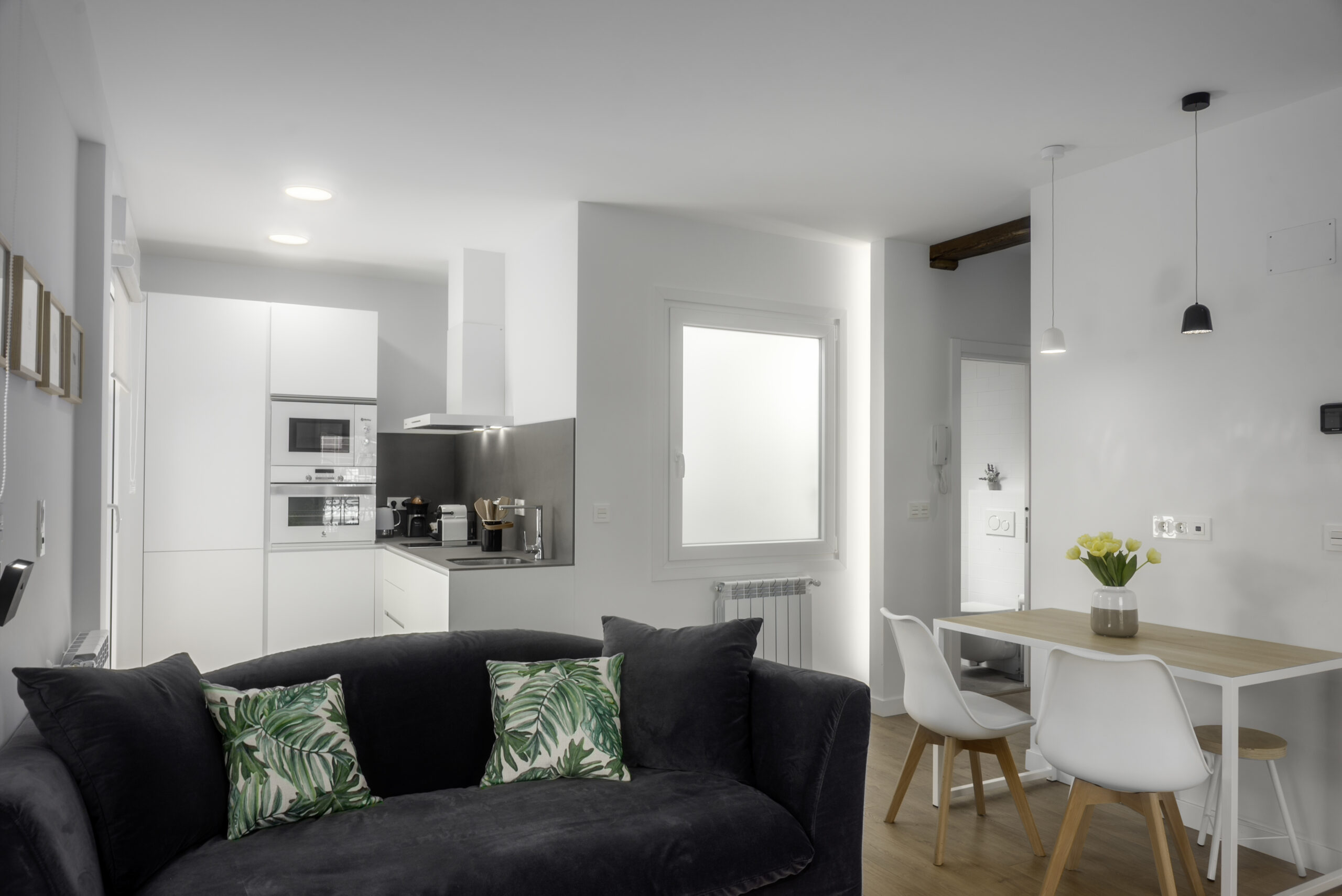 Salón con cocina integrada y sofá negro, reforma de vivienda con pladur